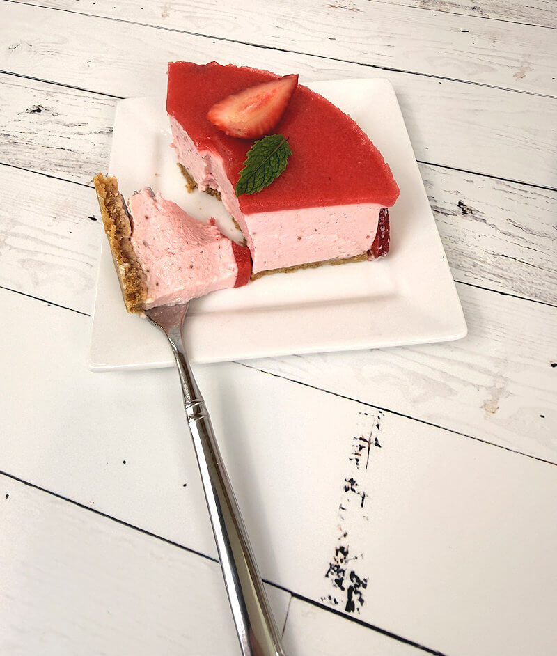 Wedge of no-bake strawberry cheesecake with piece eaten off.
