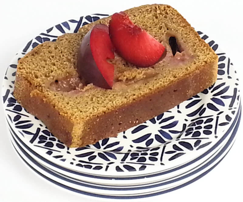 Slice of Cardamom cake with wedges of red plum on top.