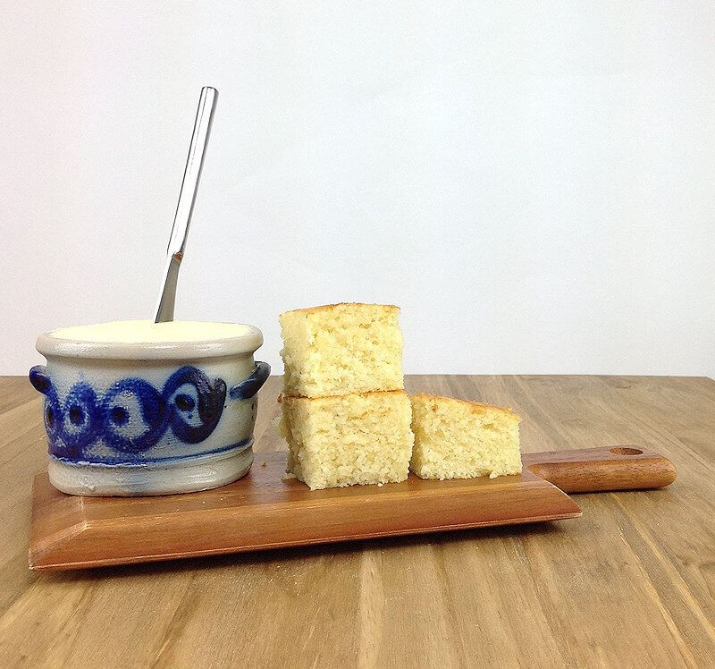Angle shot of small wooden plank with butter dish and 3 cubes of cornbread