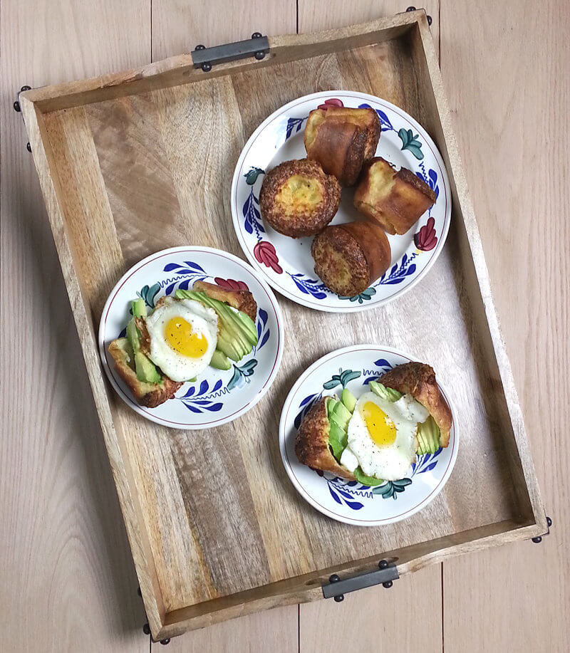 Serving tray with 3 plates. One with popovers and two with popovers cut open and dressed with avocado and fried egg.