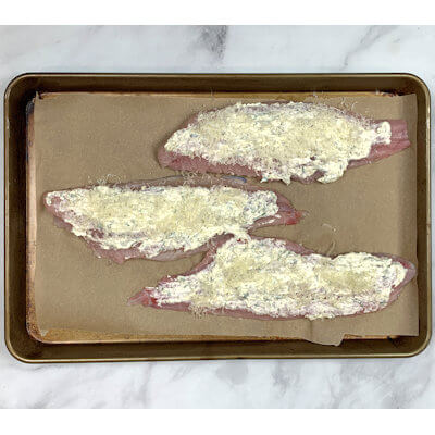 Step 2 - Place the catfish fillets on a baking sheet lined with parchment paper. Sprinkle with salt and pepper and divide the Parmesan and herbs spread over the fillets. Cover with some cheese and place the baking sheet in the oven.