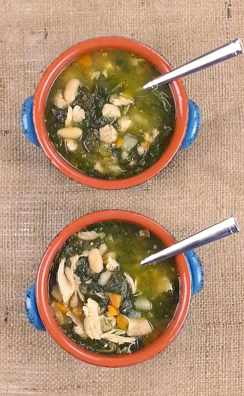 Two bowls of chicken soup with potatoes and white beans with spoons