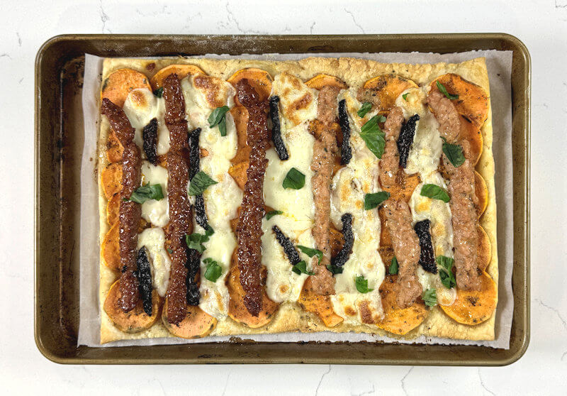 Baked Sweet Potato Slab Pie, with chorizo sausage on the left side and chicken sausage on the right side.Tear fresh basil leaves and sprinkle them over the pie.