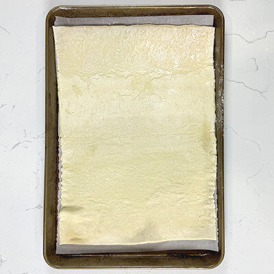 Step 1 - Line a quarter baking sheet with parchment paper. Thaw one sheet of pastry dough and roll it out to fit your baking sheet. Place the pastry dough on top of the parchment paper.