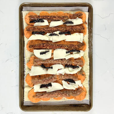 Step 4 - Divide the mozzarella in between the sausages. Not on top of the sausages, you want the meat to cook well and become crunchy. Place pieces of sun-dried tomatoes on top of the Mozzarella.