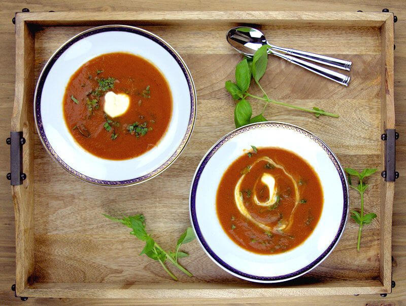 Two plates of tomato soup on a wooden try.