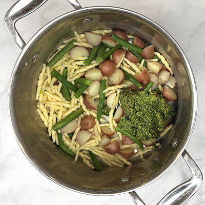 Step 3 - Drain the pasta water (keep some in reserve) and return pasta, potatoes and green beans back into the pan. Add the basil pesto.