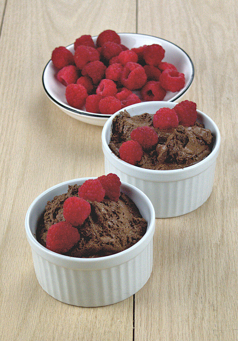 Two ramekins with ultimate chocolate mousse and decorated with raspbrries