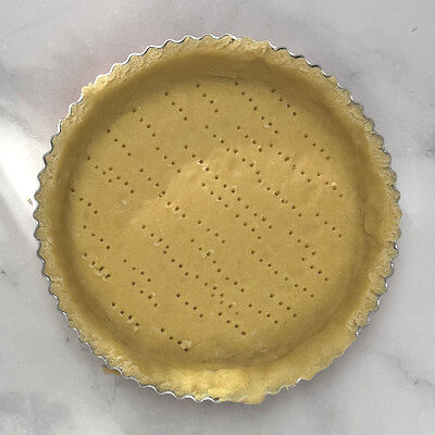 Step 4 - Grease a 6-inch quiche-form or any other from with butter and dust with flour. Take the dough out of the fridge and roll it on a flour dusted counter into a circle of approx. 7.5 inches and transfer it to the 6-inch quiche form, covering bottom and sides. With a fork punch some tiny holes in the bottom to prevent that from rising. 