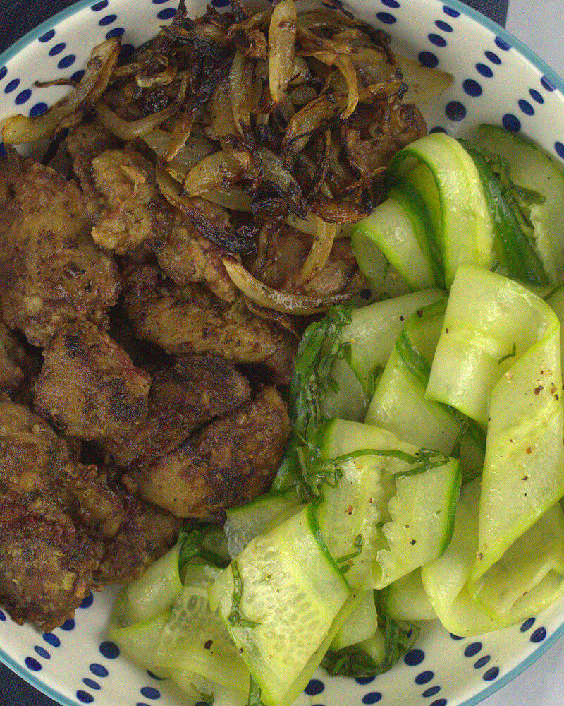 Close-up of chicken livers in bowl with sauteed onions and cucumber ribbons.