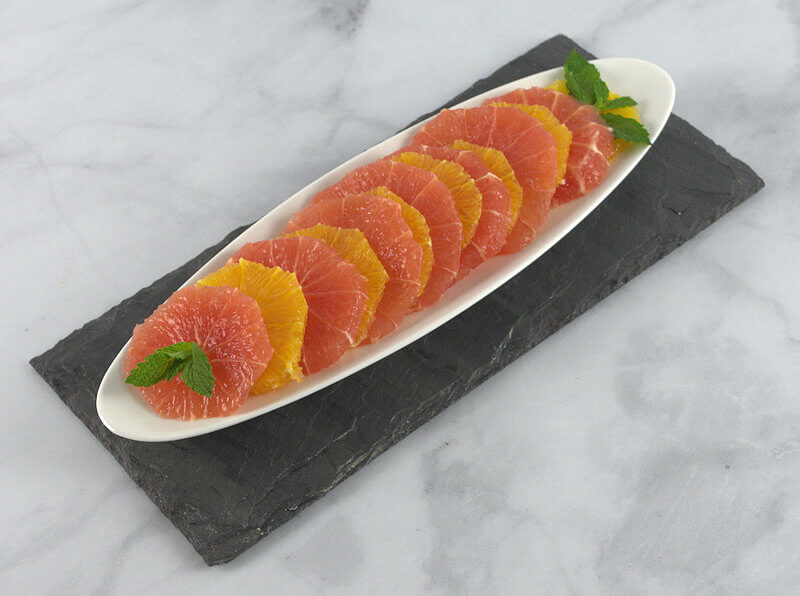 White oval shaped plate with alternating slices of grapefruit and orange, dressed with mint.