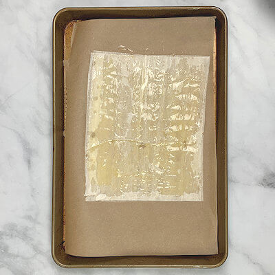 Step 2 - Place the first sheet of phyllo dough on the parchment paper. Thinly brush the phyllo dough with melted butter and place the next sheet on top and brush with butter again.