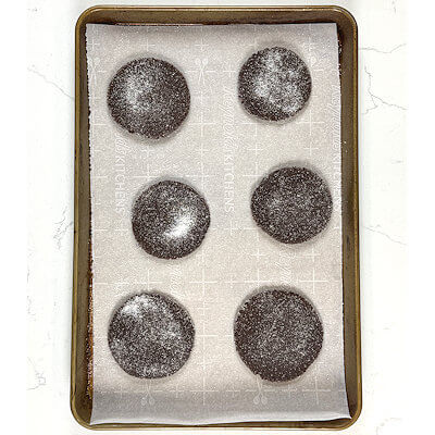 Step 6 - Roll the scoops of cookie dough with your hands and roll them in the sugar until all sides are covered. Transfer them onto a baking sheet lined with parchment paper. Flatten cookies to about 2 inches, using a glass or a spatula. Make sure they are about 2 inches apart. Sprinkle with a little bit of sugar.