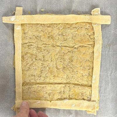 Step 2 - When the dough comes out of the oven, press the puffiness flat. Brush the egg wash (whisking the egg with 1/2 tablespoon of water) on the outer 1-inch perimeter. Top that brushed perimeter with the unbaked strips of dough (the egg wash acts as a glue). Cut off the excess on the corners. and then brush those strips with egg wash again.