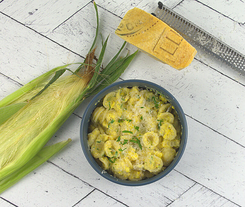Fresh corn orecchiette with hunk of Parmigiano Reggiano cheese, grater and husks of a corn