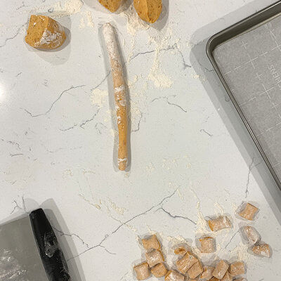 Step 3 - Take the dough out of the fridge, dust the counter with flour. Work in manageable portions. E.g. cut the dough ball in 4 parts. Roll each part into a long rope. Here you can decide how big you want your gnocchi to be; the thicker the rope, the bigger your gnocchi pillows. I rolled until the rope was about 1-1.5 inches thick. Then cut the rope into 1-inch pieces and you just created your first gnocchi.