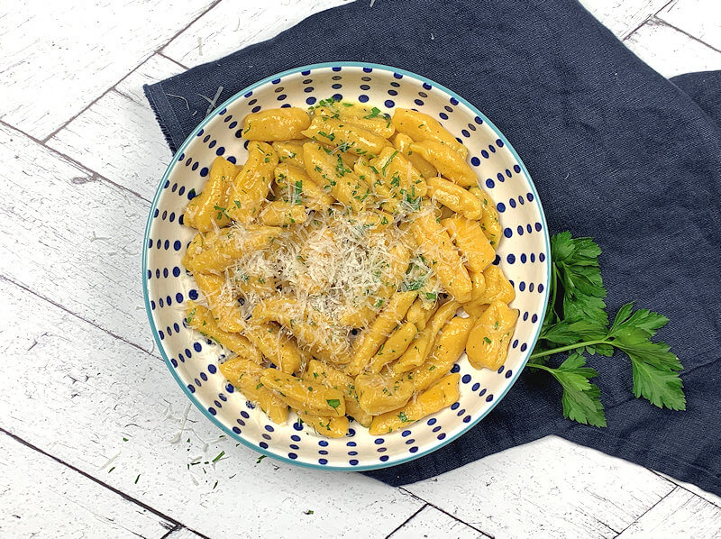 Bowl with golden beet gnocchi, sprinkled with parsley and grated Parmigiano Reggiano cheese.