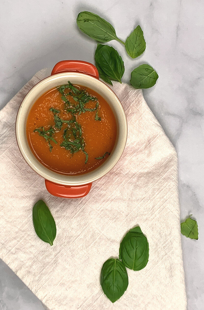 Bowl of Caribbean Citrus Tomato Soup for Two on white cloth with some basil leaves.