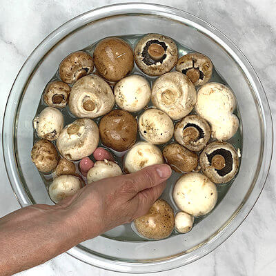 Step 2 - Fill a bowl with water and transfer the mushrooms into the water. Use your hands and wash the dirt of the caps and shortened stems.