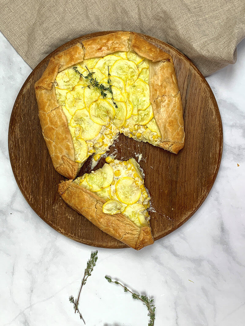 Cut Corn and Summer Squash Galette on round wooden board.