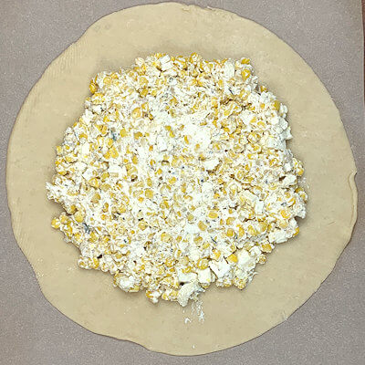 Step 3 - Unroll pie dough onto parchment paper and place that on a baking sheet. Spread cheese-corn mixture onto the dough, but leave about 1.5-2-inch perimeter uncovered.