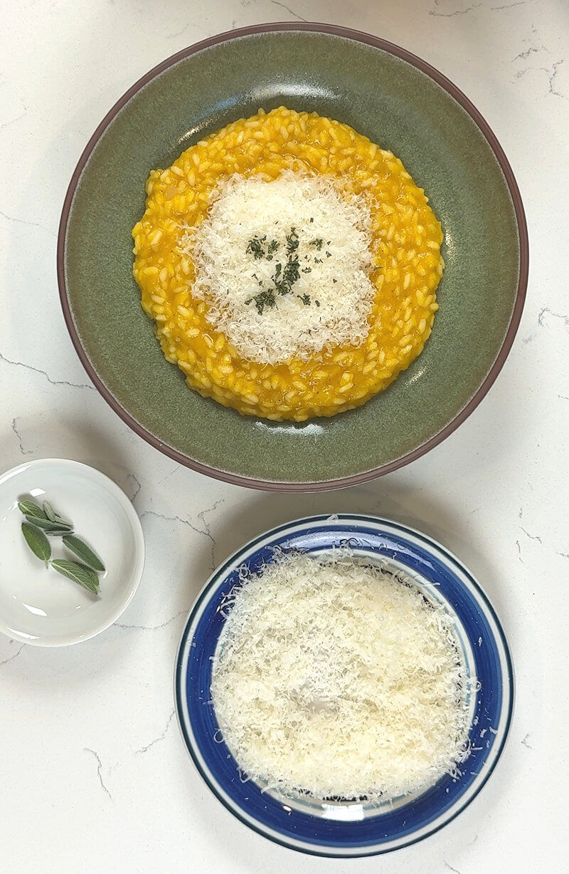 Green dish with Butternut Squash Risotto and separate plates with sage leaves and grated cheese.