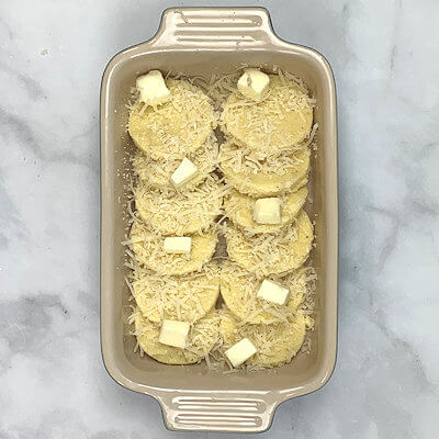 Step 7 - Fill a baking dish with semolina discs, each overlapping the previous. You can reshape the scraps and make more discs. Sprinkle some grated cheese over the discs as well as little dollops of butter.