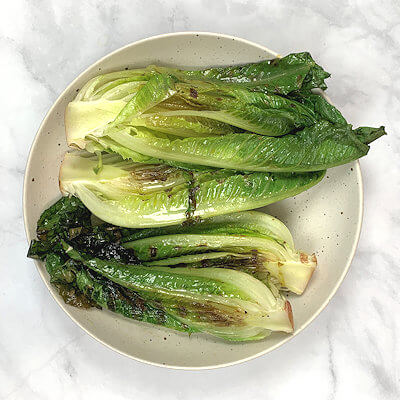 Step 5 - Cut the romaine lettuce in half (keep the core attached and quickly grill the lettuce halves in the same grill pan or on the grill. Since there is still oil in the grill pan, no need to add more. Grill just a few minutes on each side. You will see the end of the leaves wilting, but the core of the lettuce remain juicy.
