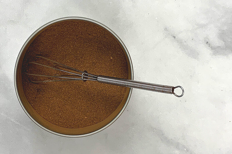 Metal tin with all ingredients mixed. Small whisk sticking out.