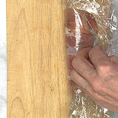 Step 5 - Use the plastic wrap to lift the Prosciutto off the board and pull over the meat. Finish the roll completely, and twist the ends tight.