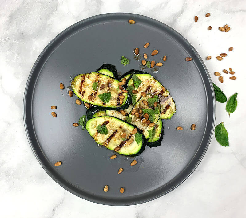 Top down image of plate with grilled zucchini, pine nuts, mint and dressing.