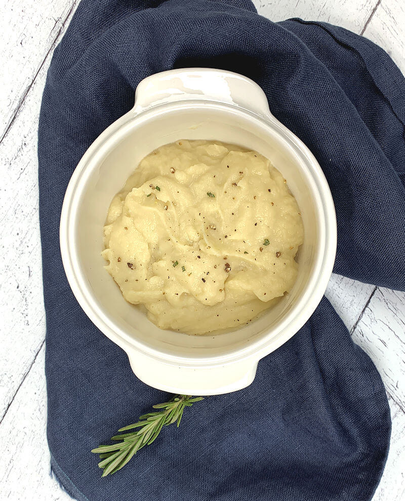 Smooth parsnip puree in white bowl on dark blue cloth.