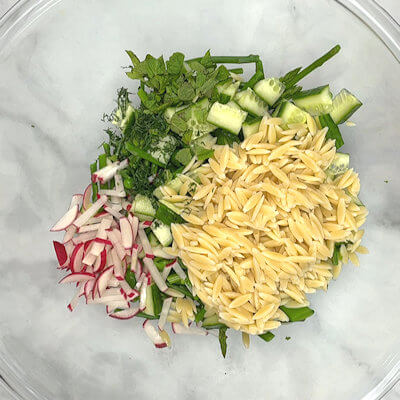 Step 6 - To a large bowl, add asparagus, green peas, snap peas, radishes, cucumber, herbs, and orzo. Pour dressing on top and mix.