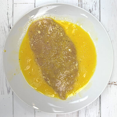 Step 2 - Whisk an egg on a plate and coat the floured chicken cutlets with the egg. Again both sides.