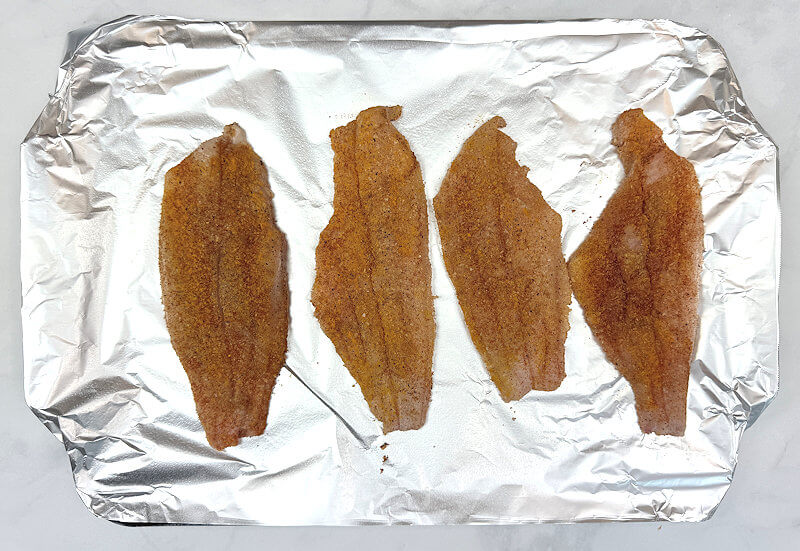 Tray lined with aluminum foil and 4 catfish fillet rubbed with spices.