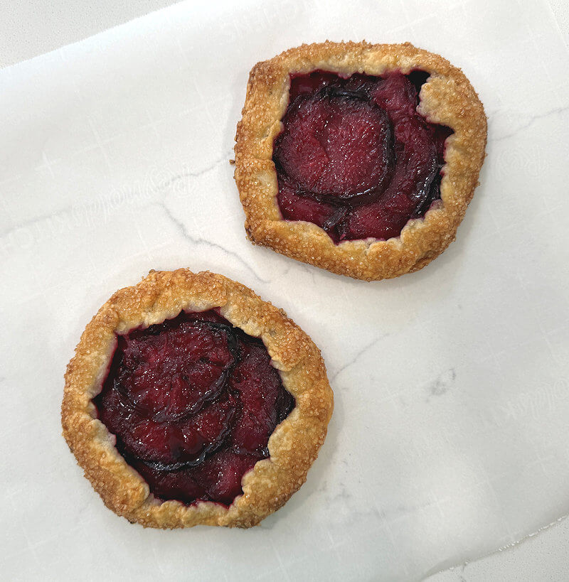Two baked mini plum galettes on parchment paper.