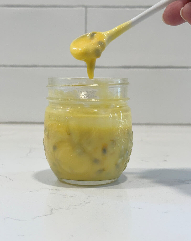 Passion fruit curd slowly dripping off a spoon