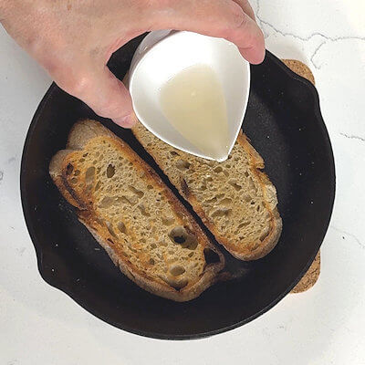 Step 1 - Toast two slices of rustic bread, white or whole wheat. Make sure you have sturdy slices as they will hold a lot of cheese. Place the slices in a oven-safe skillet or a baking sheet and drizzle them with white wine.