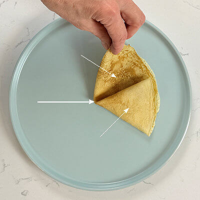 3. The 1/3 fold. Fold a crêpe in half, creating a half moon. Fold the half moon 1/3 of the way up and then fold the other side over the already creating triangle.