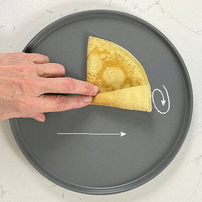 5. Cone roll. First fold the crêpe in half, creating a half moon. Then place a finger in the middle of the straight line and roll the outside from right to left, forming a cone.