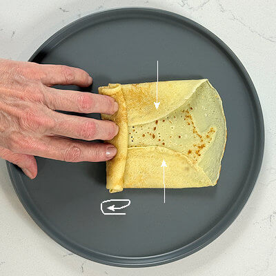 6. The 'Burrito roll'. First bring the left and right edges toward the center, partially covering the fillings. Roll the bottom part of the crêpe over the fillings, while keeping the sides tucked in. Roll until it you reach the other side.