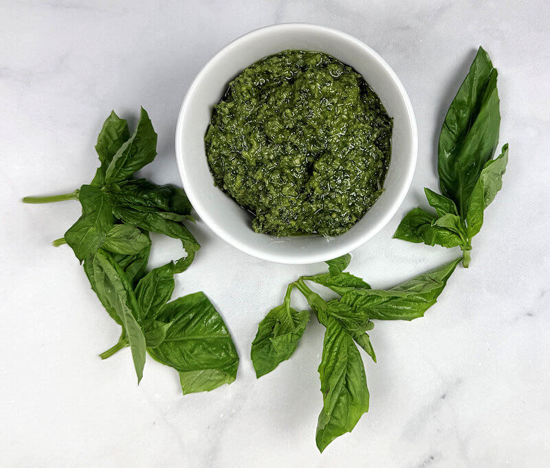 White bowl with basil pesto, surrounded by basil leaves