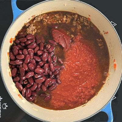 Step 5 - Add the remaining ingredients: red kidney beans, crushed tomatoes, tomato paste and beef broth. Mix and bring to a simmer.