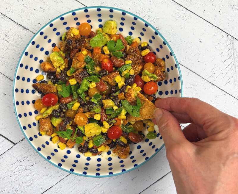 Hand scooping cowboy caviar with chicken out of a bowl with a tortilla chips
