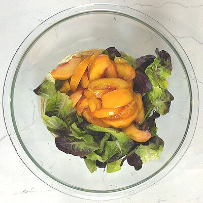 Step 4 - Add butter lettuce and peach slices into the bowl with the dressing and give it a quick mix.