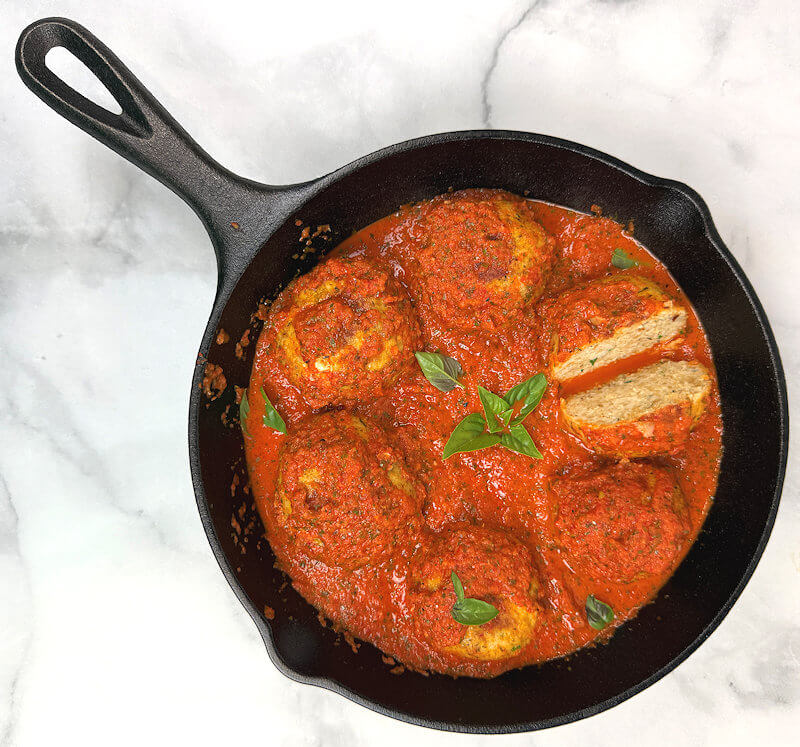 Cast iron skillet with 6 Chicken Meatballs with Red Pepper Sauce. One meatball is cut in half.