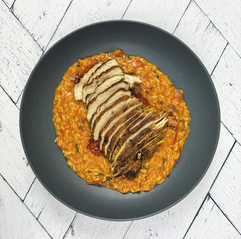 Tomato risotto served with chicken on top.