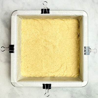 Step 2 - Spread crumble in the baking pan, lined with parchment paper (6x6 inches) and use a small measuring cup or spoon to press it into an even layer across the bottom. Bake the bottom for about 10 minutes in a 350°F oven.